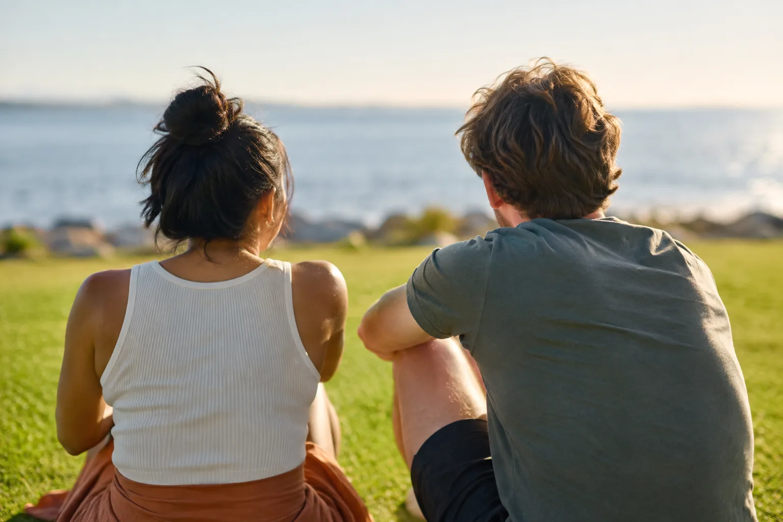 Friends relax on a sunny public lawn near the waterfront, chatting and enjoying a casual afternoon outdoors.