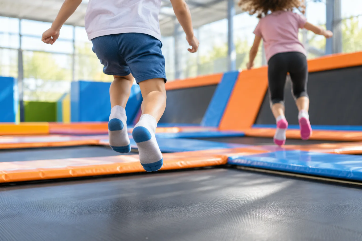 Children jumping on interconnected trampolines inside a bright, spacious indoor recreation park.
